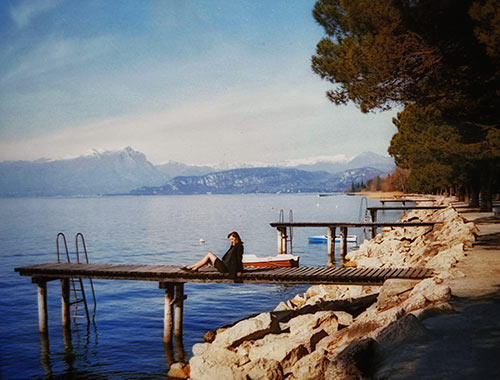 Eine junge Frau sitzt auf einem hölzernen Bootssteg am Ufer des Gardasees.