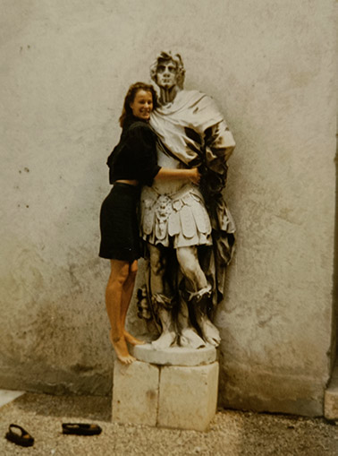 Eine junge Frau umarmt scherzend eine steinerne Männerstatue in Verona.